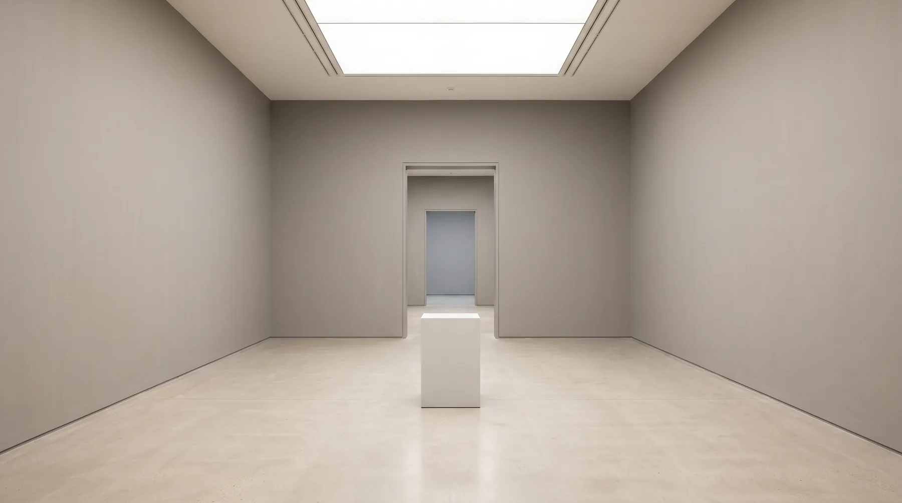 An empty gallery with warm grey walls and a pale concrete floor, a single empty white plinth under a skylight, and a doorway leading to further rooms.