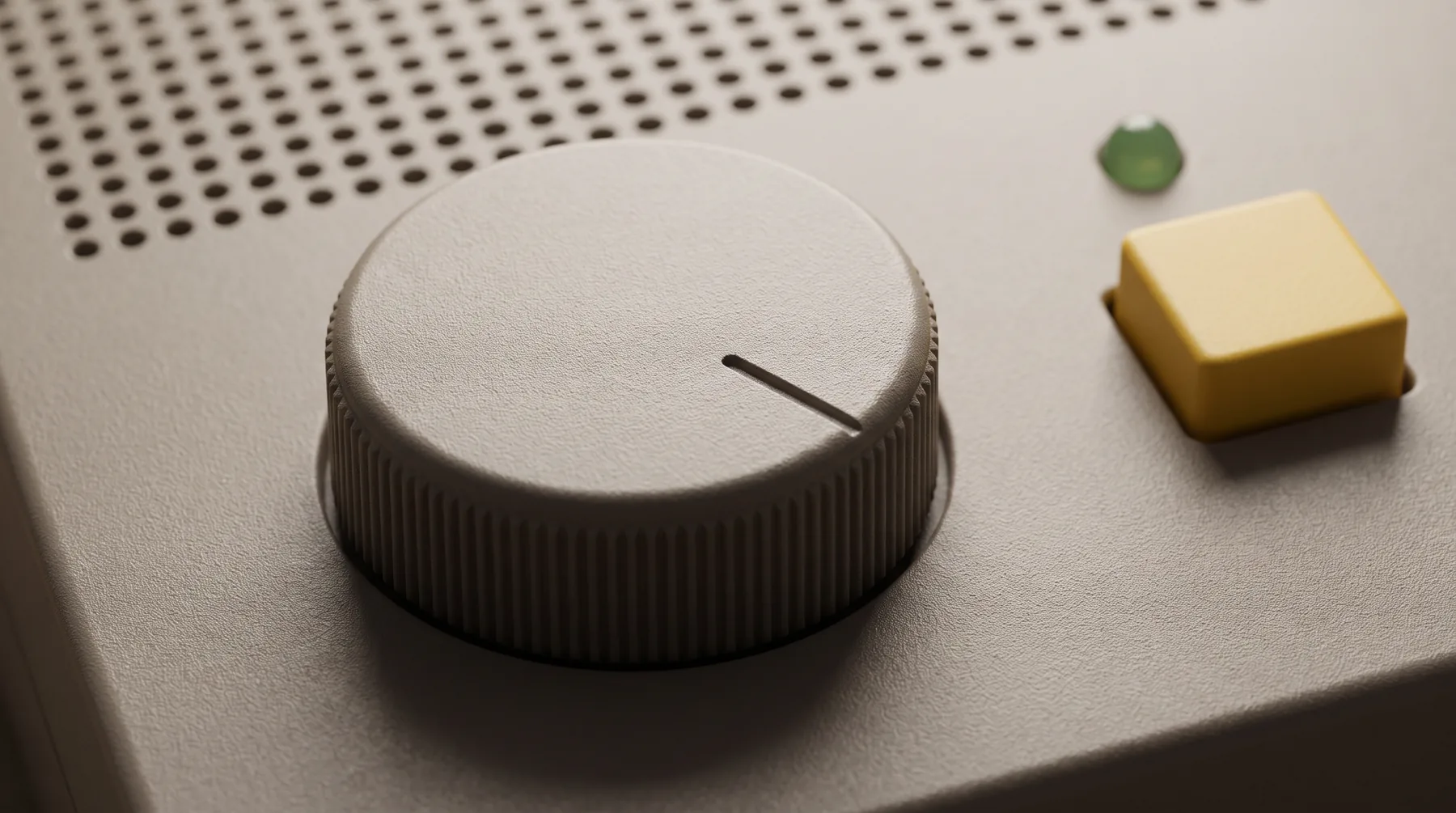 Close-up of a knurled warm grey dial with a thin pointer line, a yellow square key and a small green lamp beside a field of speaker holes.