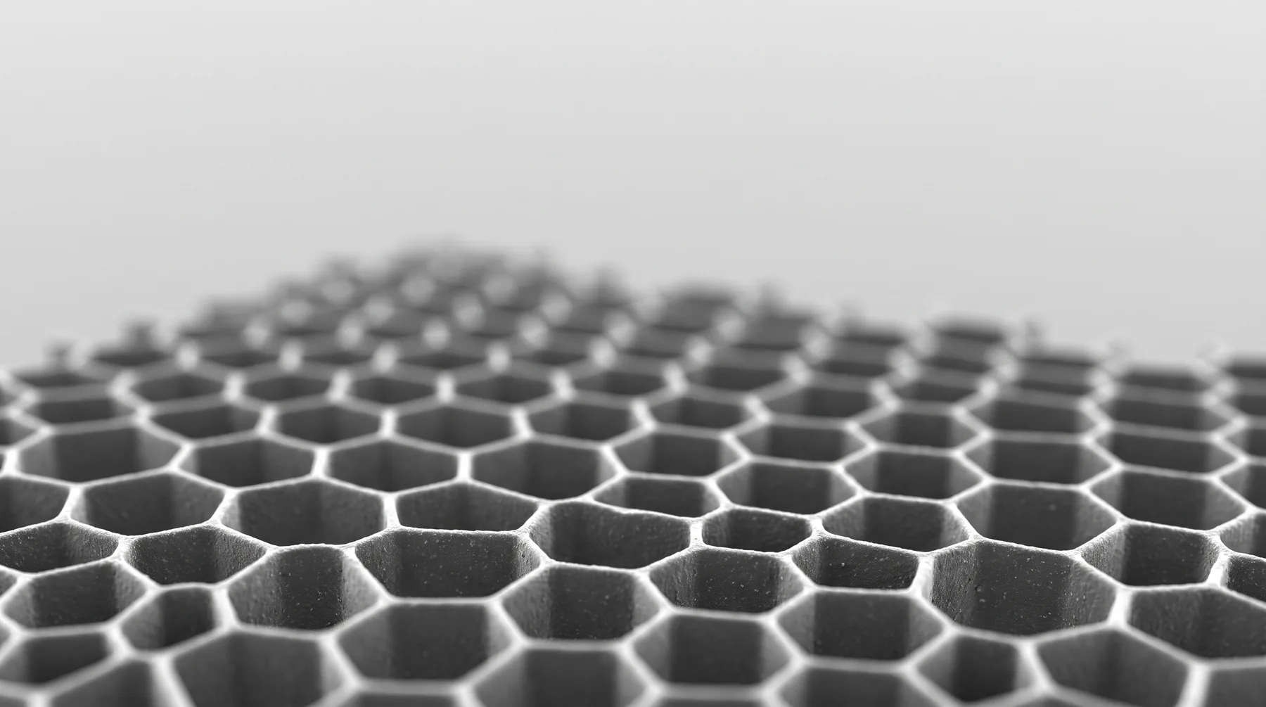 A grayscale, electron-microscope-style view of a regular honeycomb lattice, sharp in the foreground and softening into the distance.